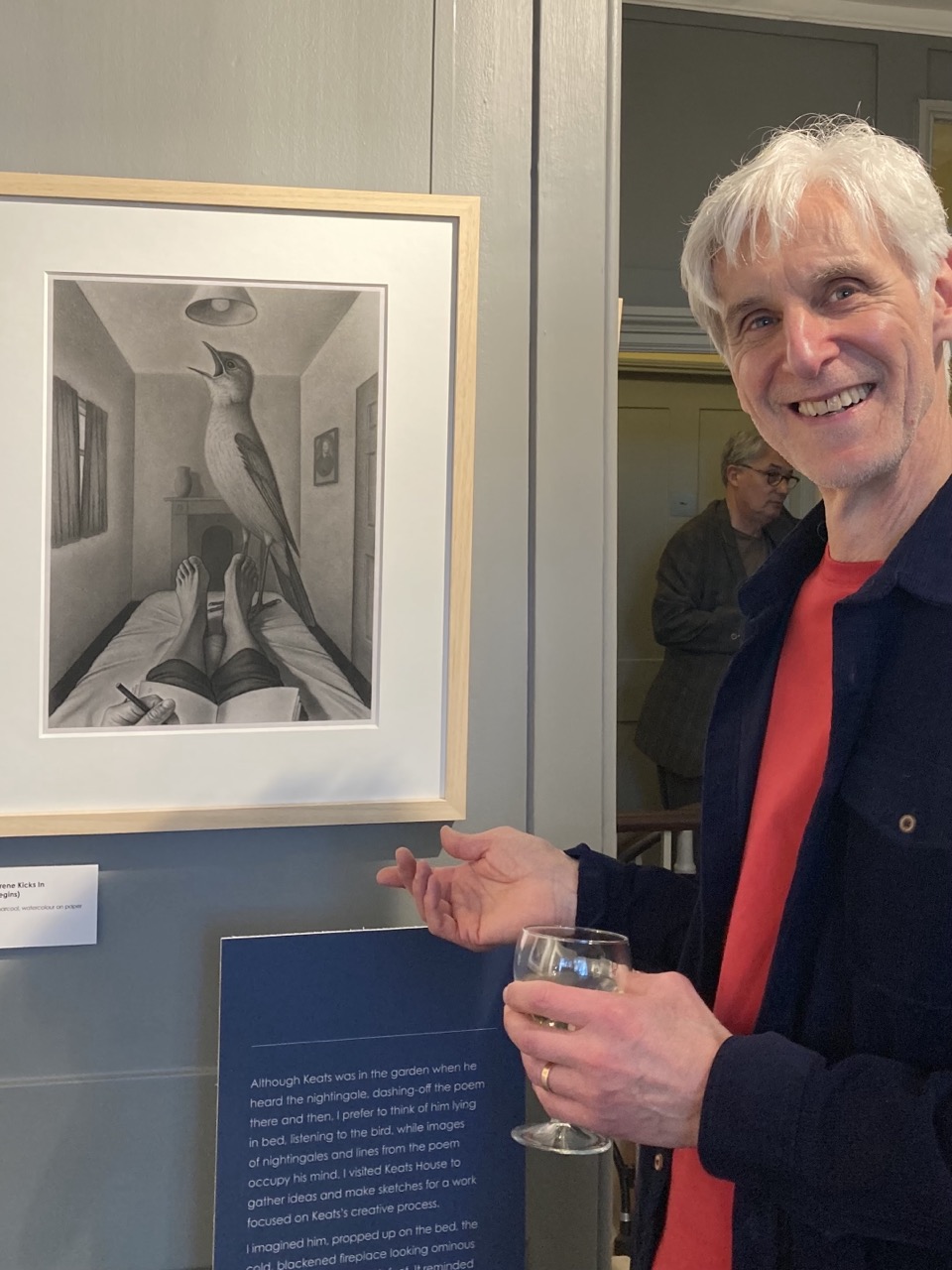 Martin Huxter standing in front of the picture of a figure in bed with a large nightingale at his feet.