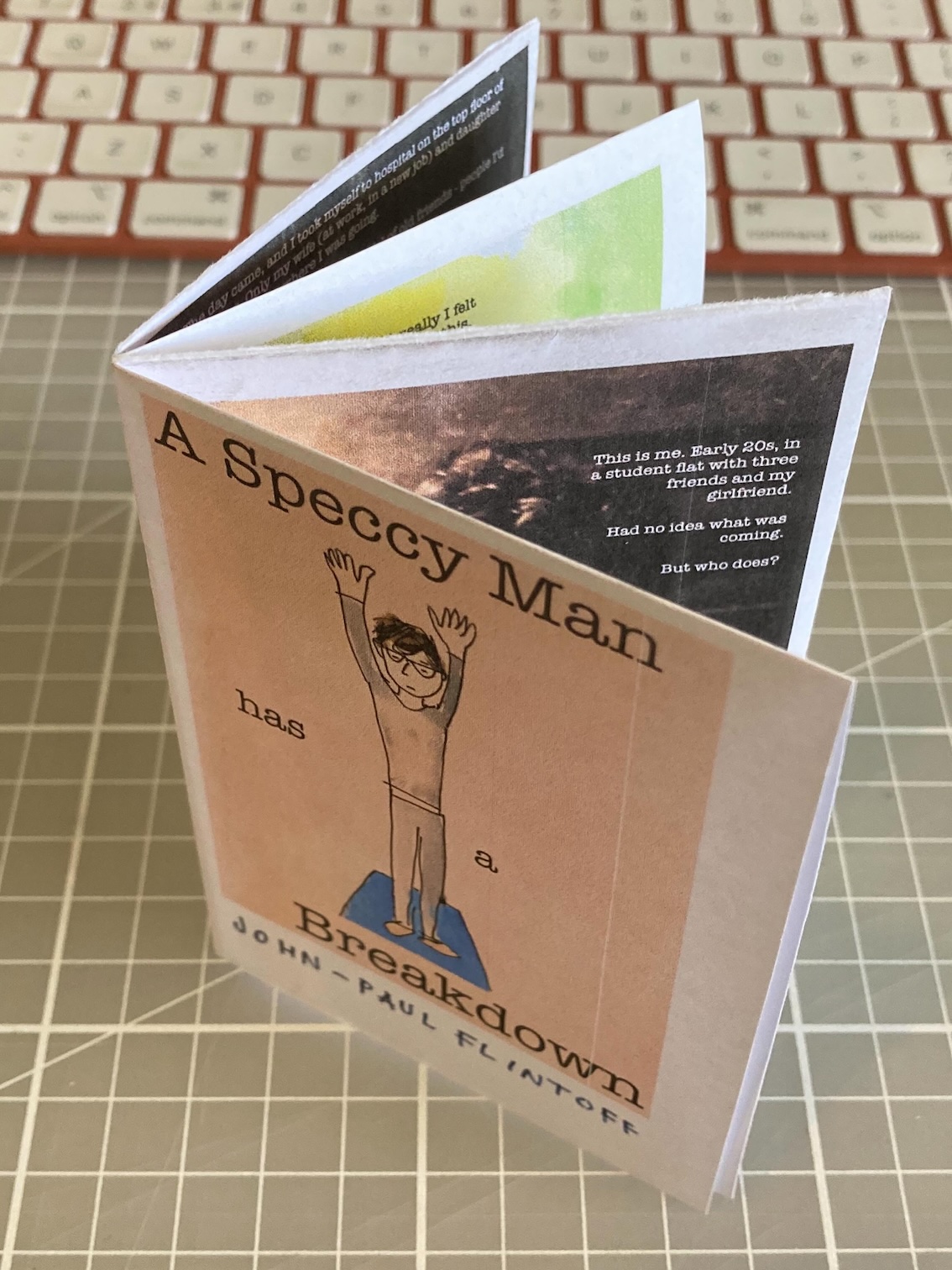 Eight-page zine, standing on a cutting mat, with pink front cover reading A Speccy Man Has A Breadown, over a drawing of a man doing a sun salute. Eight-page zine, standing on a cutting mat, with pink front cover reading A Speccy Man Has A Breadown, over a drawing of a man doing a sun salute.
