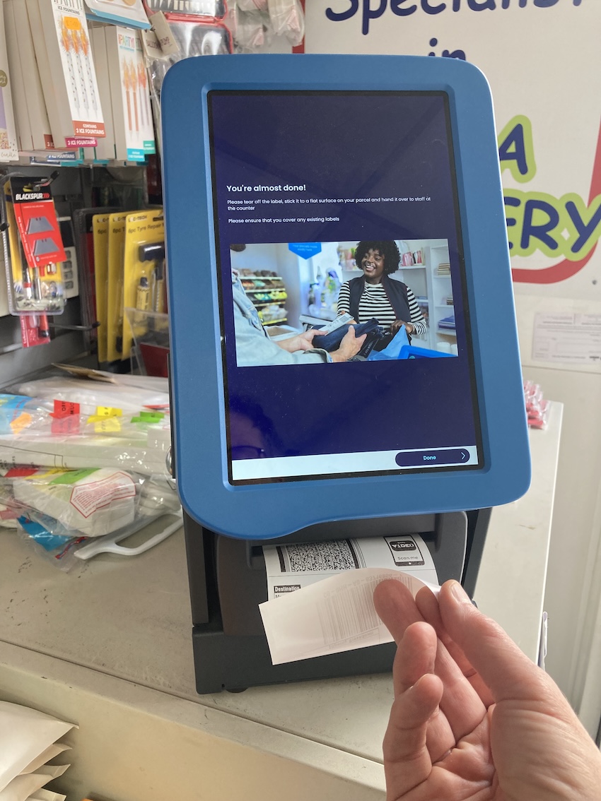 Hand reaching for printed label from same Evri machine, this time screen reads 'You're almost done!' Hand reaching for printed label from same Evri machine, this time screen reads 'You're almost done!'