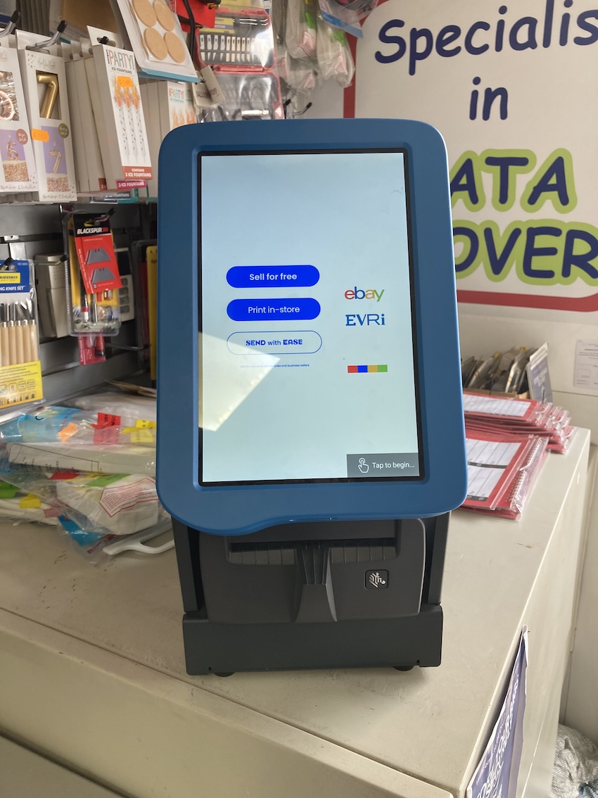 Photo of Evri postage label printer surrounded by clutter in a stationery shop, with screen waiting for a new customer. Photo of Evri postage label printer surrounded by clutter in a stationery shop, with screen waiting for a new customer.