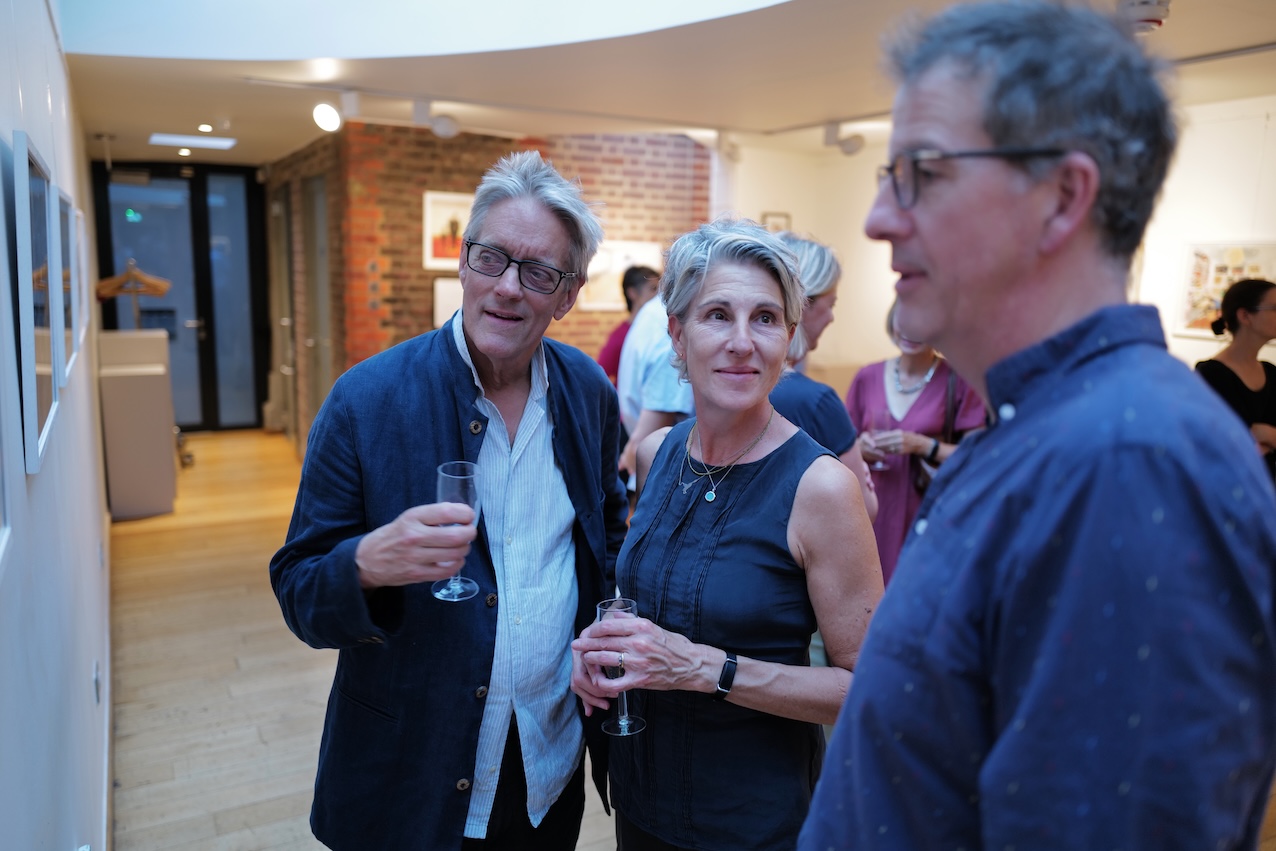 Three people with glasses of champagne in a gallery, looking at a framed picture on the wall to the left. Three people with glasses of champagne in a gallery, looking at a framed picture on the wall to the left.