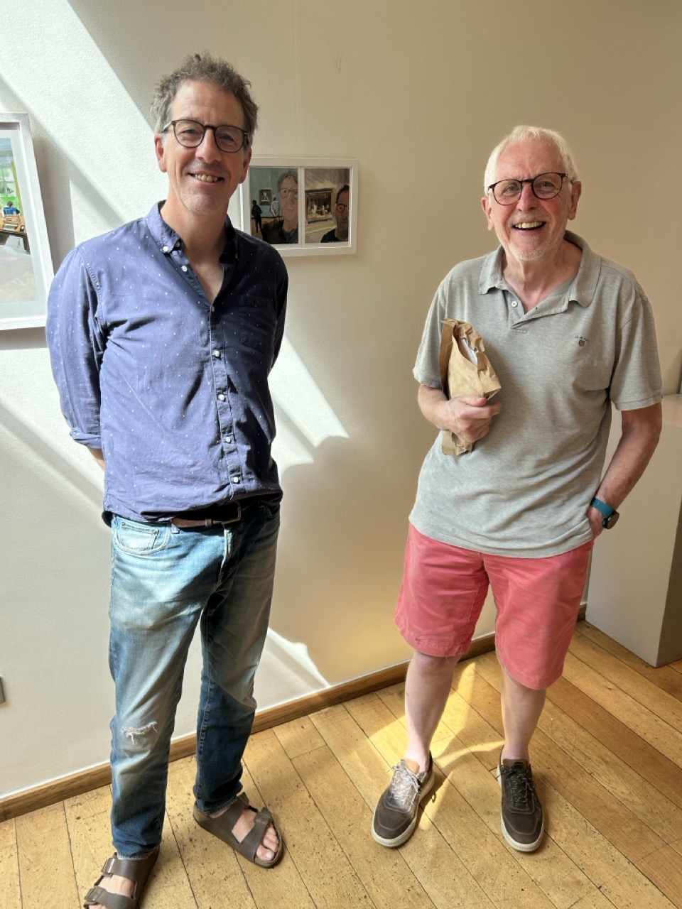 The buyer and John-Paul Flintoff standing beside a framed pair of small self-portraits at Burgh House.