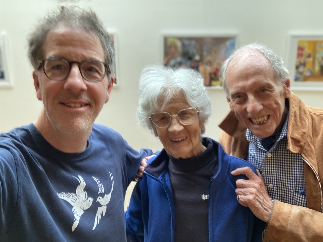 A selfie at Burgh House: me, smiling, with my mother and father, framed prints on the wall behind us.