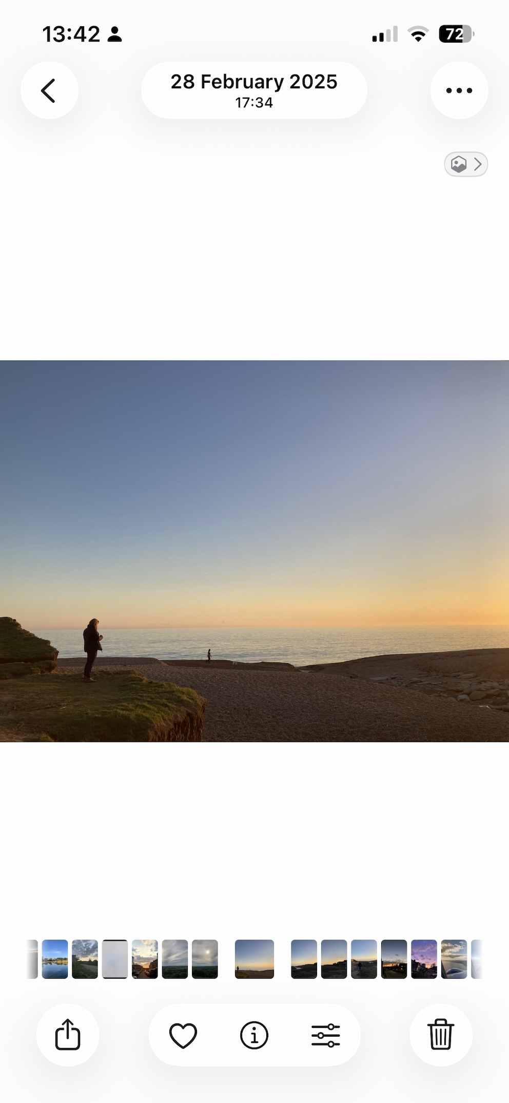 A wide sunset photo of a beach and sea open on a phone, a figure standing on a low cliff to the left A wide sunset photo of a beach and sea open on a phone, a figure standing on a low cliff to the left