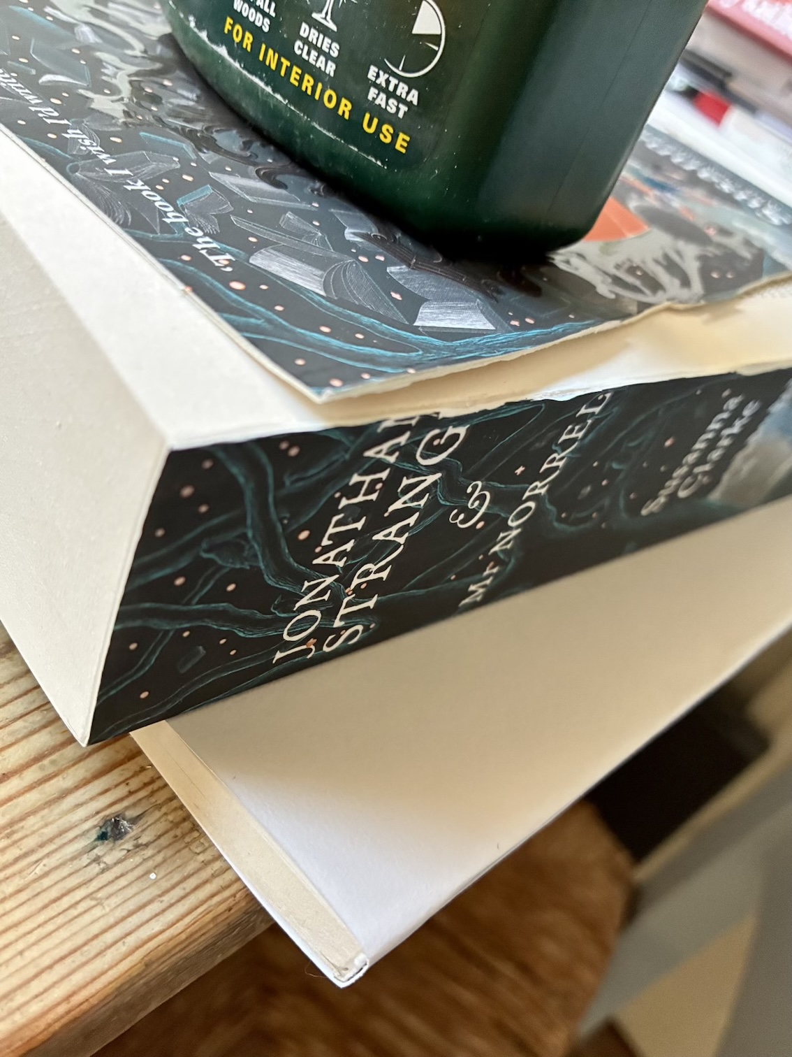 The newly covered section drying under the rest of the Jonathan Strange & Mr Norrell paperback, with a green bottle of wood glue on top for weight