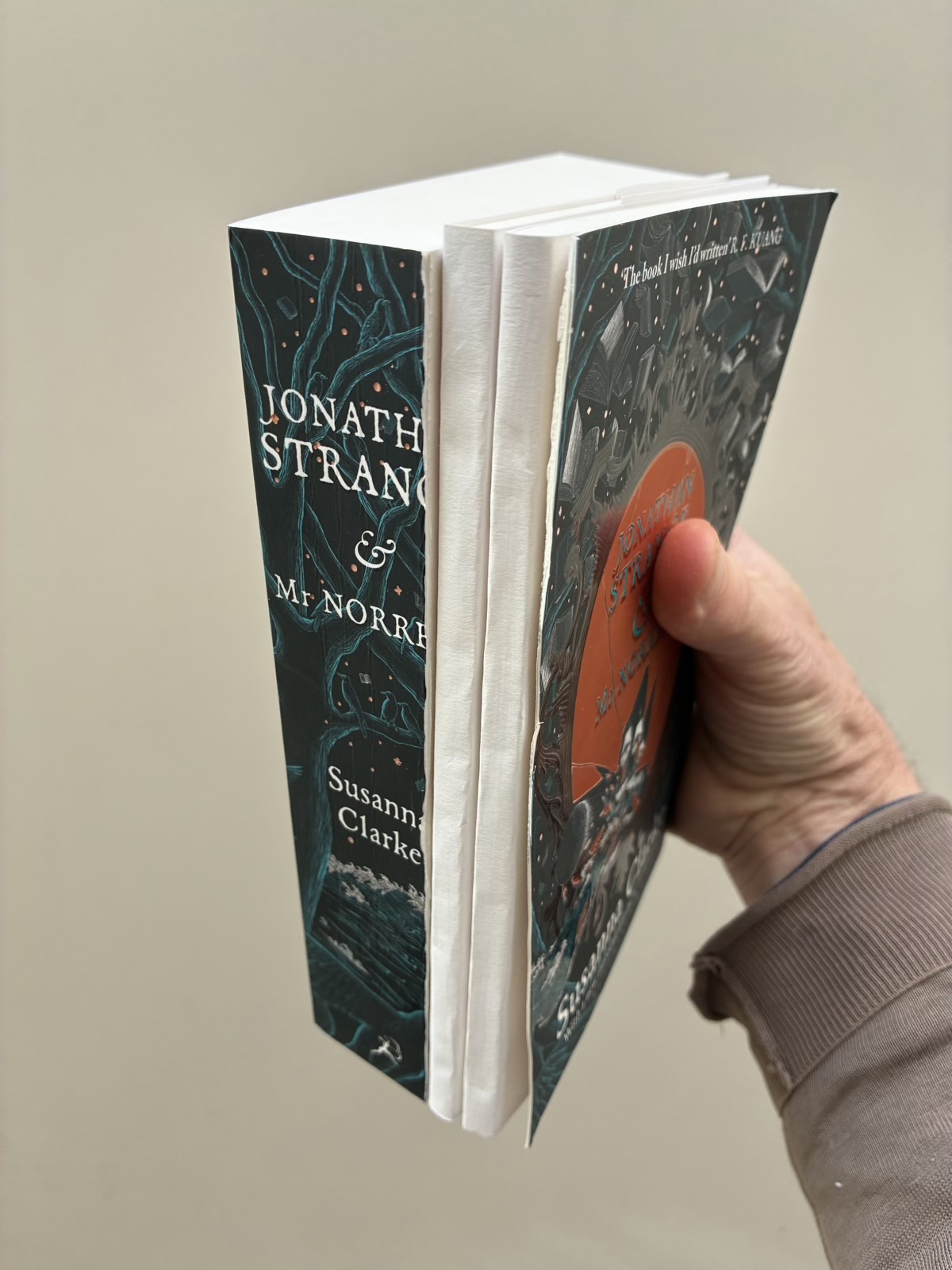 A hand holds several parts of the larger book between the separated covers.