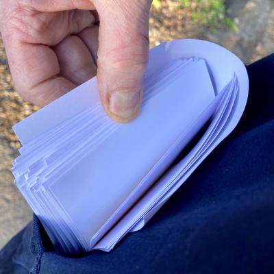Photo of my thumb flicking through many loose sheets of paper, which are sticking out of my jacket pocket.